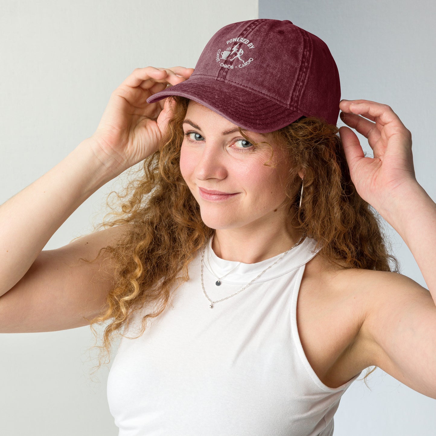 Maroon vintage cotton twill cap with white embroidered "Powered by Coffee, Chaos & Cardio" text worn by woman.