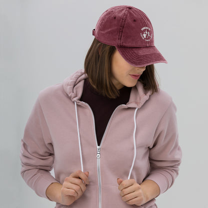 Maroon vintage cotton twill cap with white embroidered "Powered by Coffee, Chaos & Cardio" text worn by woman in mauve hoodie.