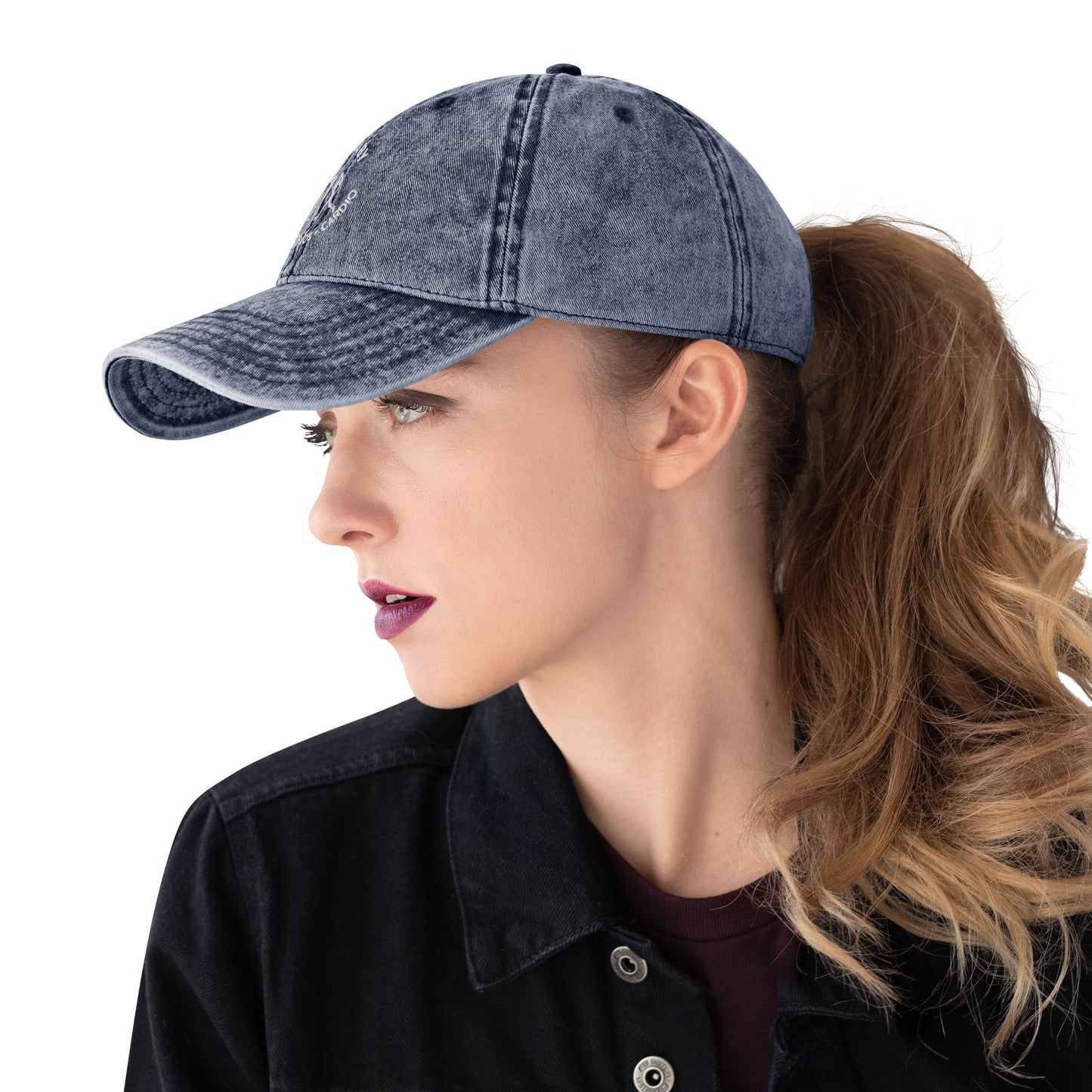 Charcoal grey vintage cotton twill cap with curved brim, embroidered slogan, worn by woman with ponytail and dark lipstick.