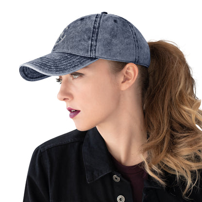 Charcoal grey vintage cotton twill cap with curved brim, embroidered slogan, worn by woman with ponytail and dark lipstick.