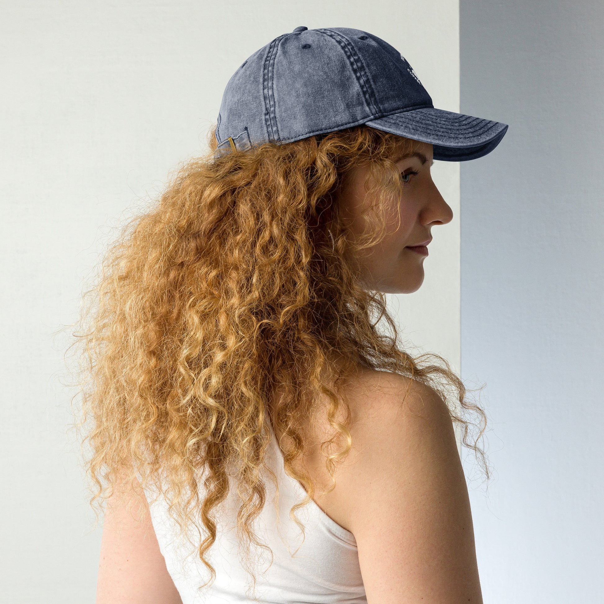 Charcoal grey vintage cotton twill cap with curved brim and embroidered slogan worn by woman with curly hair.