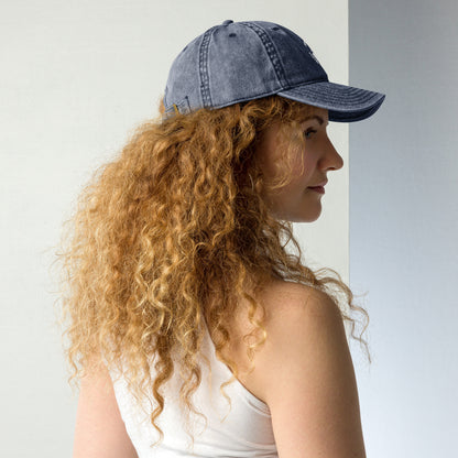 Charcoal grey vintage cotton twill cap with curved brim and embroidered slogan worn by woman with curly hair.