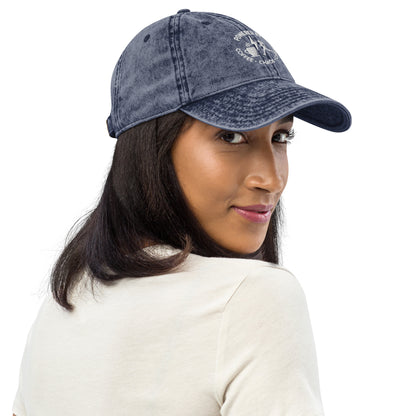 Charcoal grey vintage cotton twill cap with embroidered "Powered by Coffee, Chaos & Cardio" text, worn by woman.