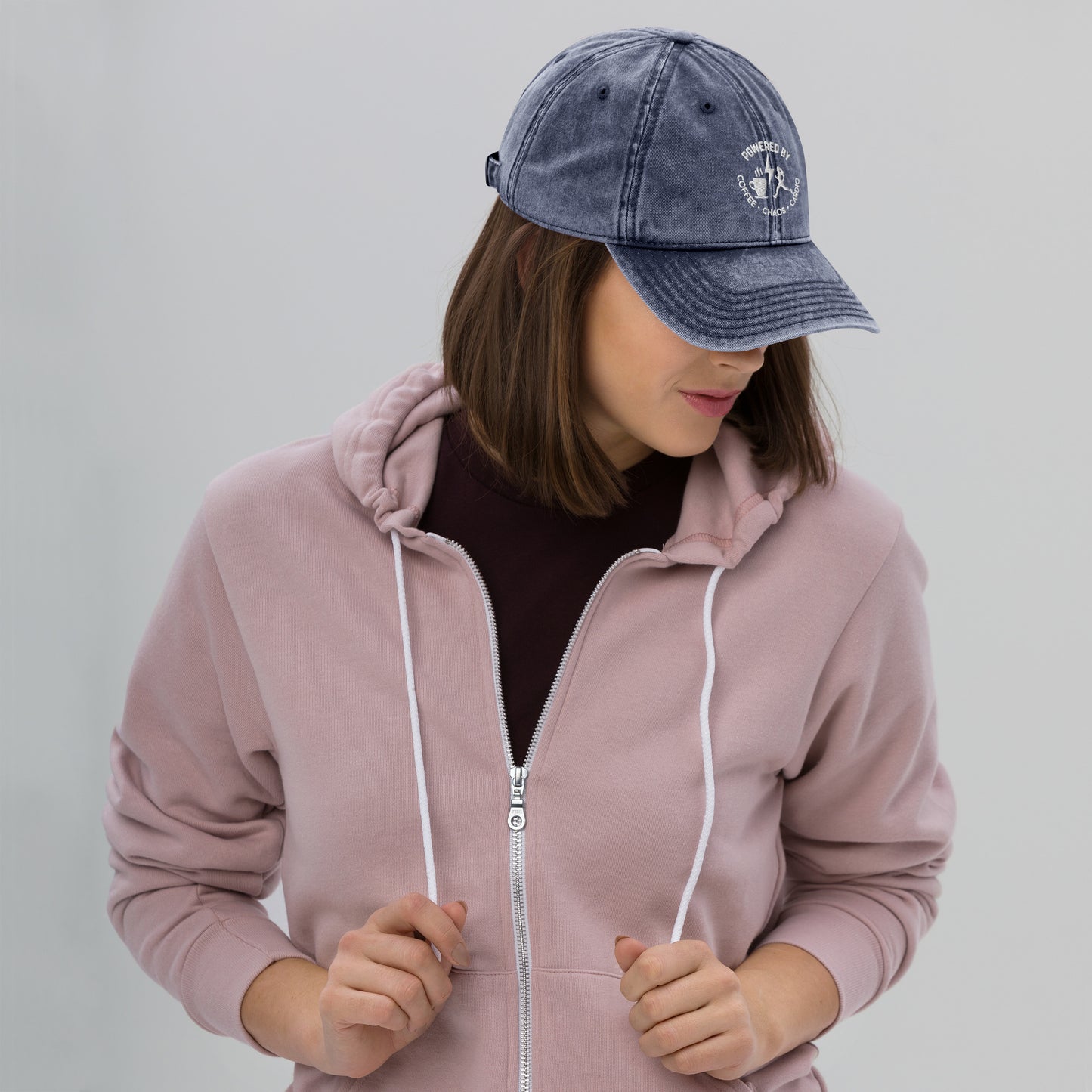 Charcoal grey vintage cotton twill cap with curved brim and embroidered circular logo on front side worn by woman in mauve.